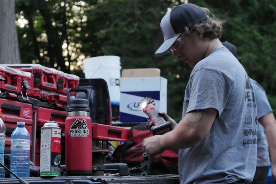 A technician cleaning a suspension component with a wire wheel at dusk