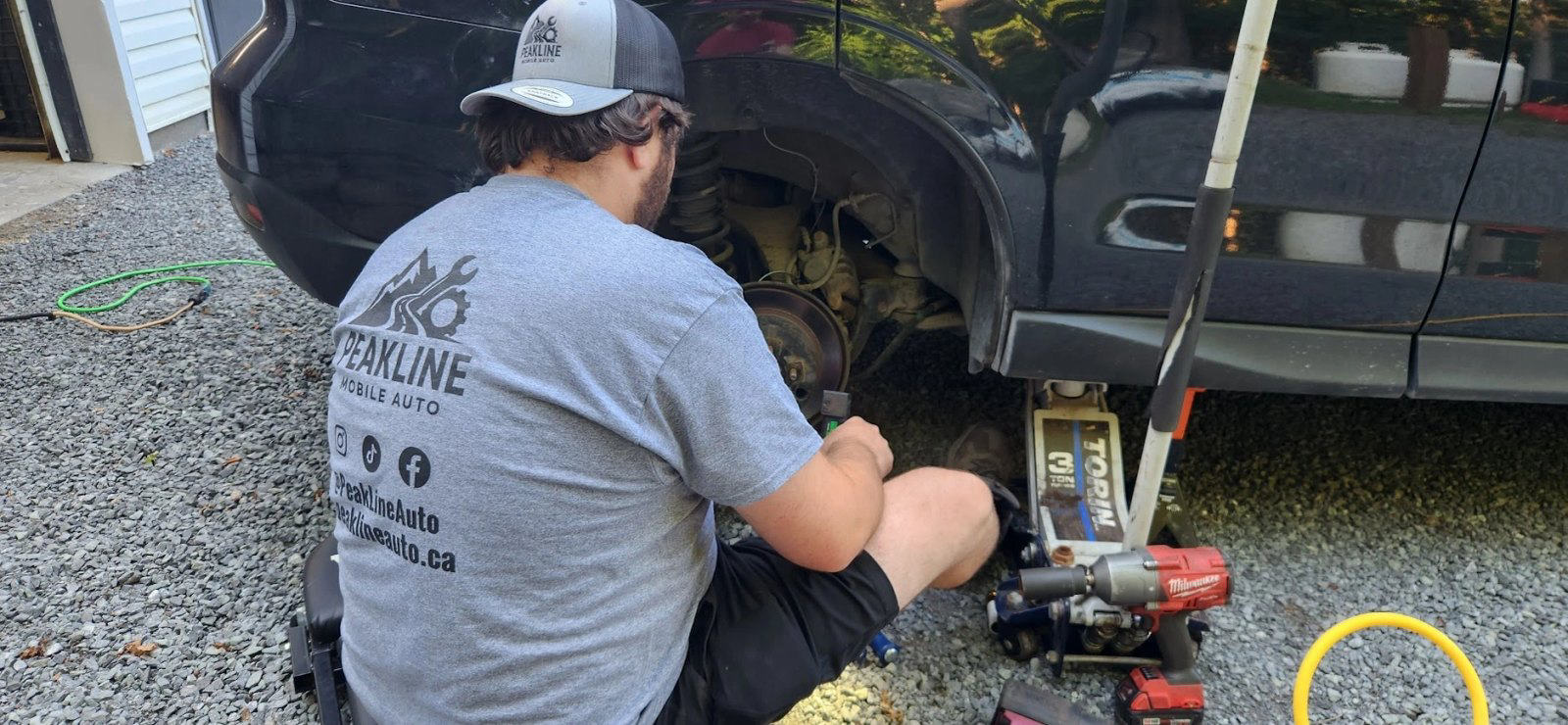 A technician with a floor jack and impact gun at the rear wheel of an SUV